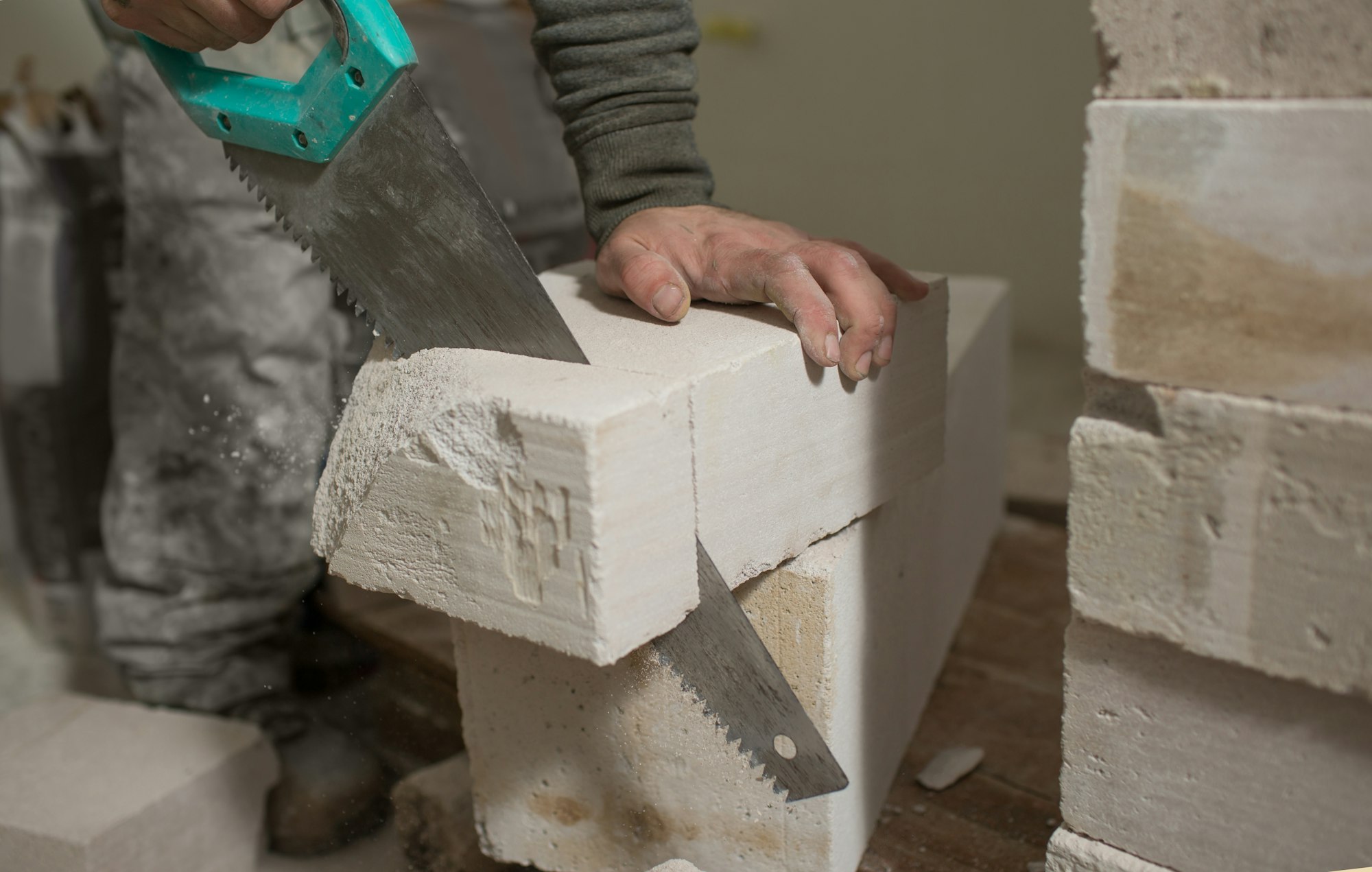 a man saws a block of foam concrete with a close-up of a hand and a hand saw.